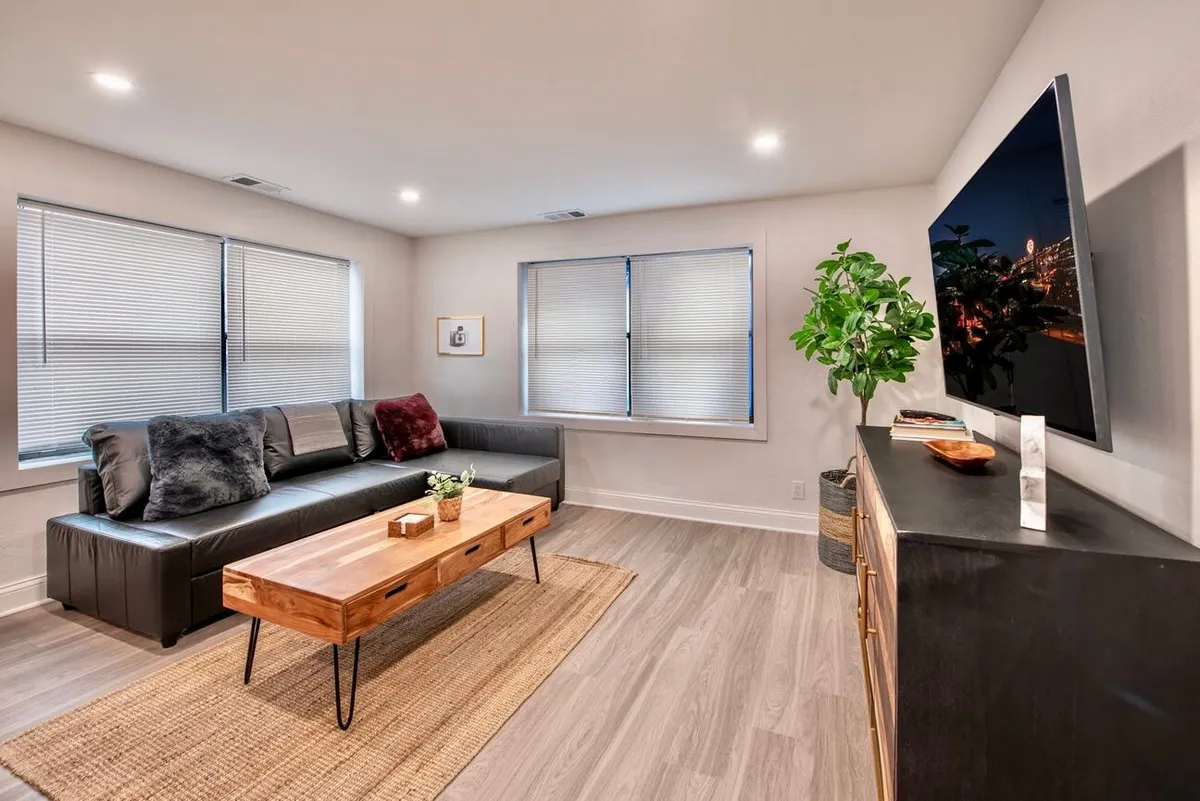 A cozy living space with a comfortable sofa, a coffee table, and a TV setup. A plant adds a fresh touch to the room, and the overall arrangement suggests a space designed for both entertainment and relaxation, with warm lighting enhancing the inviting mood.