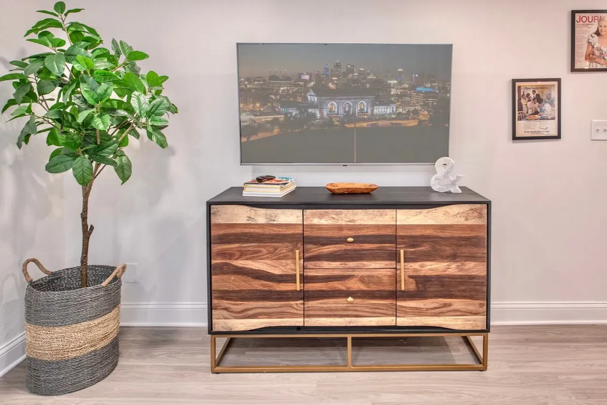 A welcoming corner featuring a wooden cabinet adorned with decorative items, an indoor plant, and cityscape wall art. This vignette adds a personal, stylish touch to the living area, suggesting an environment filled with character and thoughtful design.