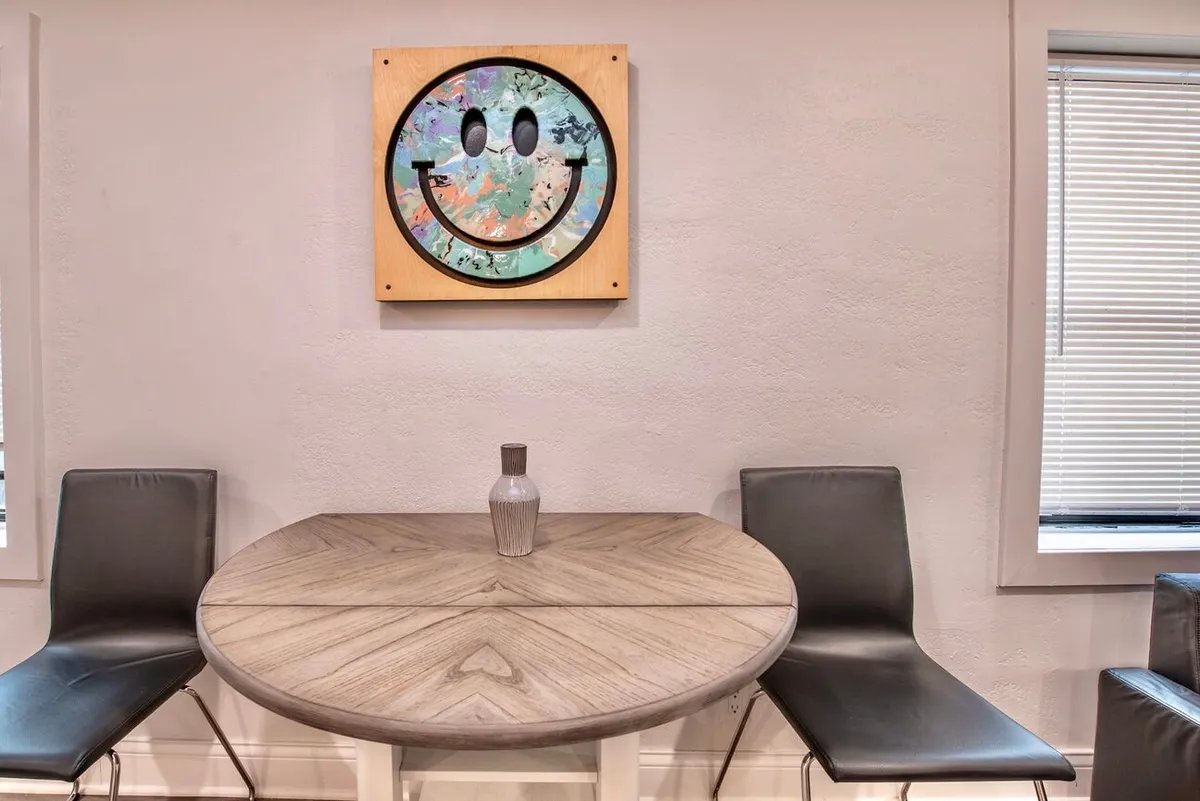 A playful and intimate dining nook scene centered on a round wooden table adorned with a vase, complemented by smiley face artwork. The mood is lively and inviting, perfect for casual dining or special occasions.